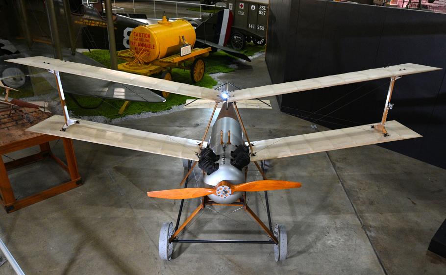 A small pilotless biplane with a wood-and-metal chassis sits on display in a museum.
