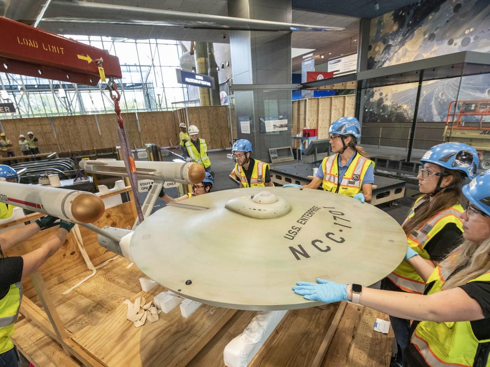 A team of people move a model of the Starship Enterprise from Star Trek.