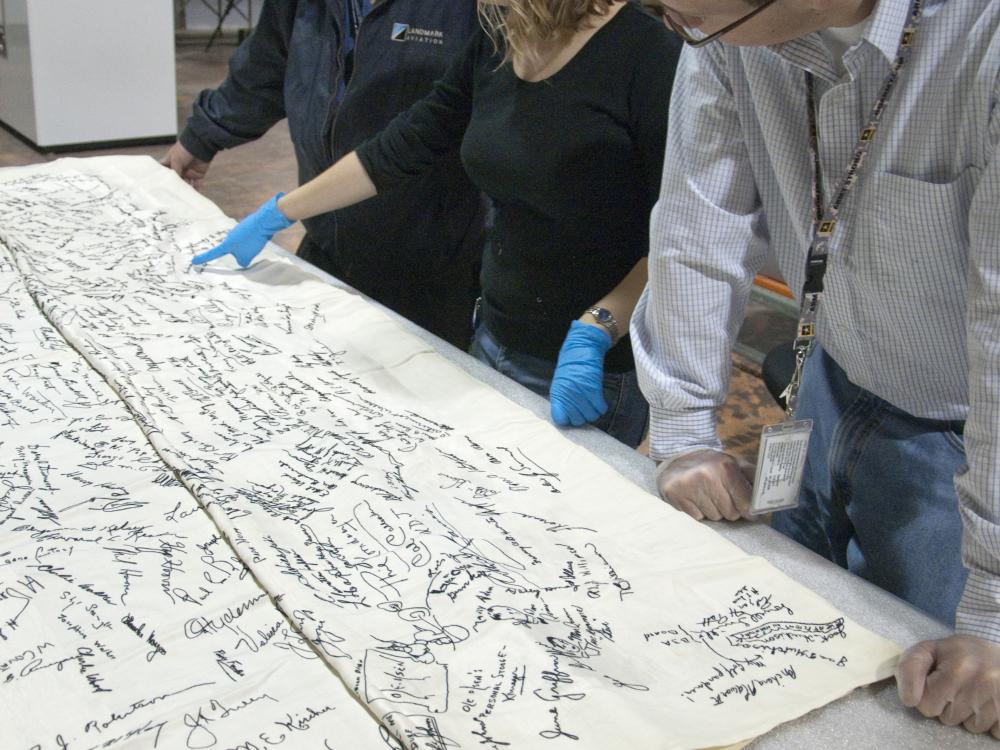 A group of people look at a signed tablecloth. 