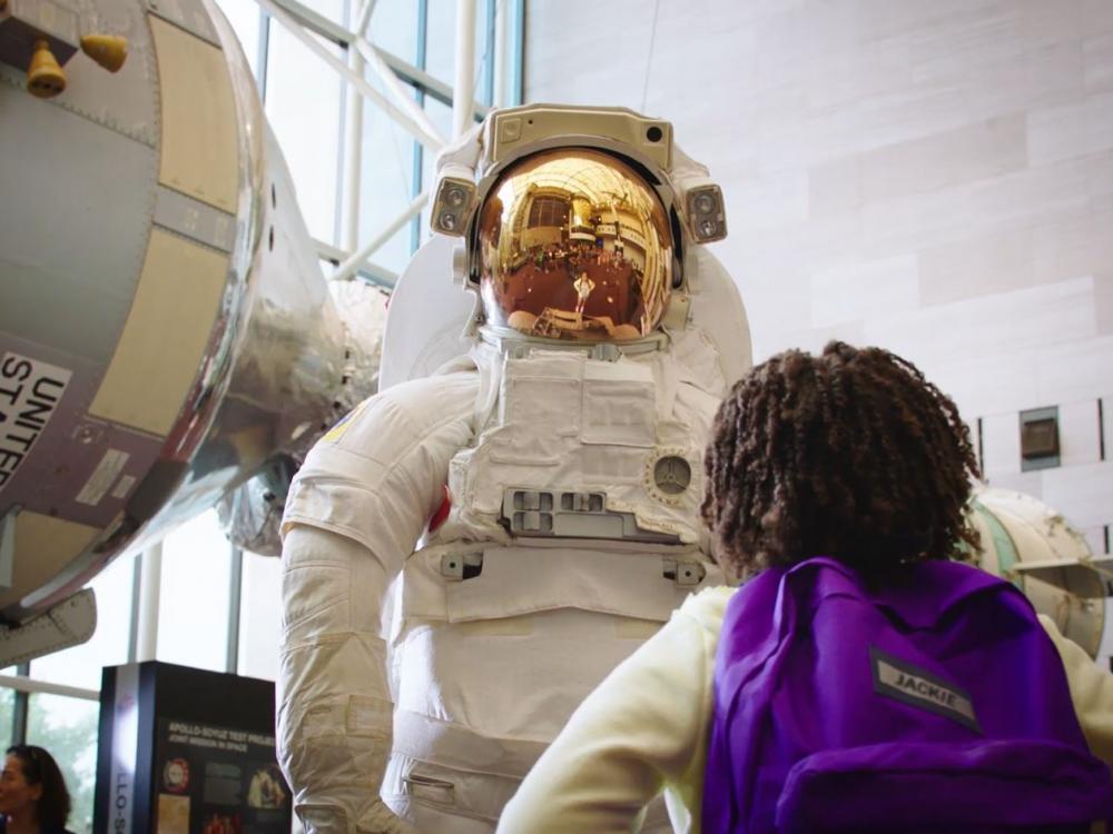 Girl looking up at astronaut suit model at the National Air and Space Museum.