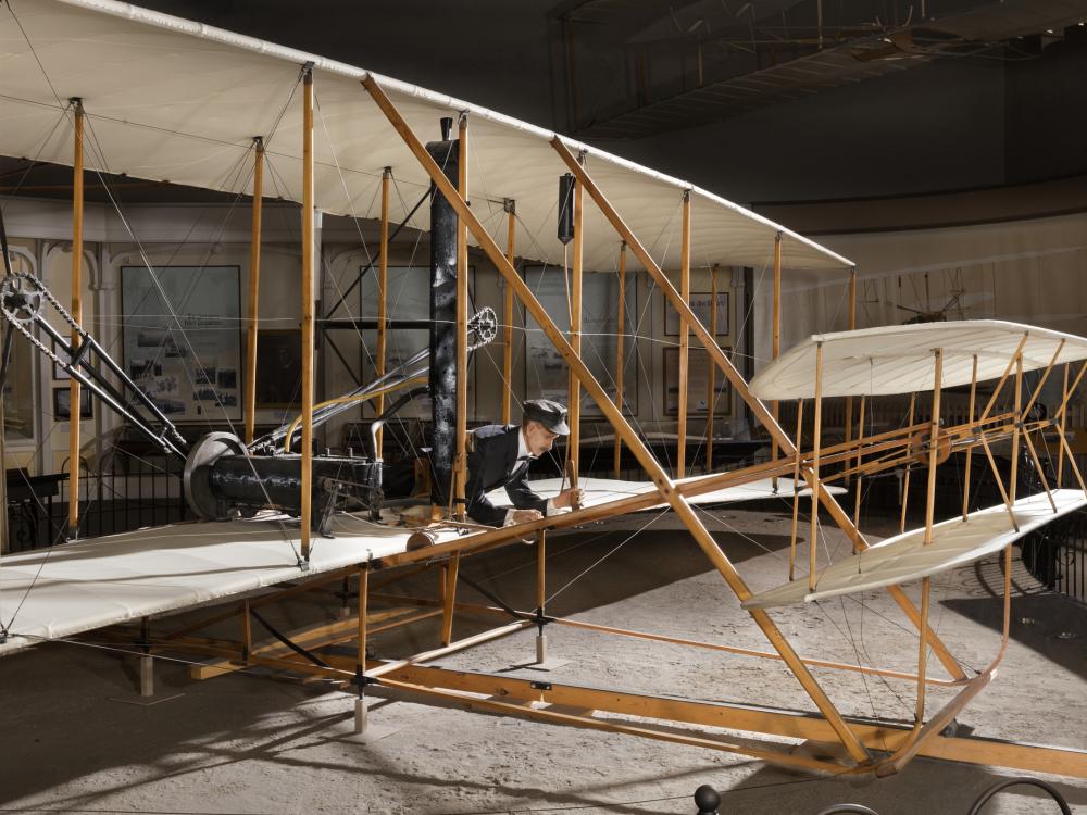 Front of 1903 Wright Flyer with model of Wright Brother laying flat in aricraft