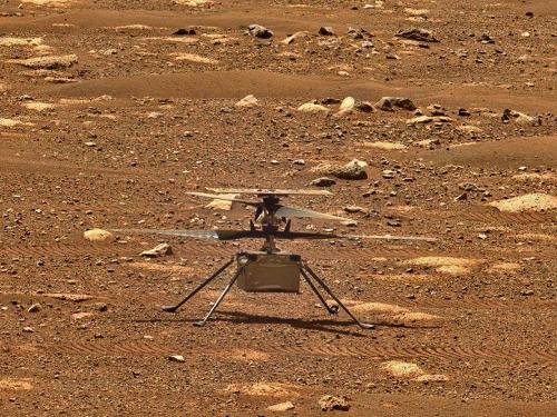 A small helicopter sits at idle on a rocky surface.