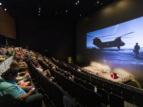 A semi-crowded theater watches a feature on Top Gun. 