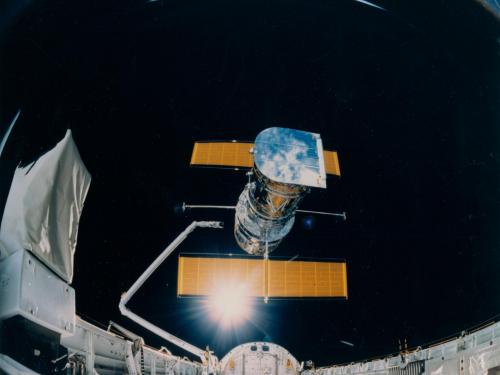 The Hubble Space Telescope, a large telescope with a set of solar panels on two sides, is deployed from the Space Shuttle Discovery.