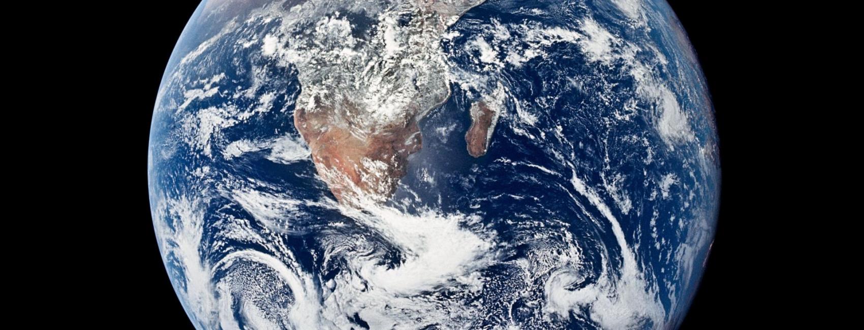 A complete circle with swirling clouds above landmasses, the Earth is seen from above. 